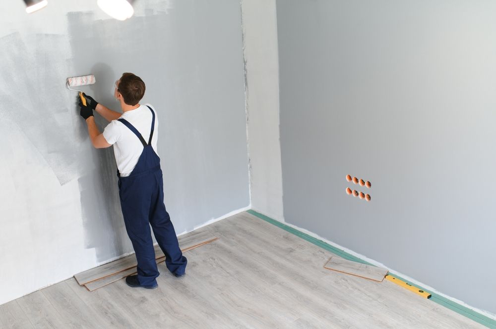 Person paints a wall with a roller. The room is partially painted gray.
