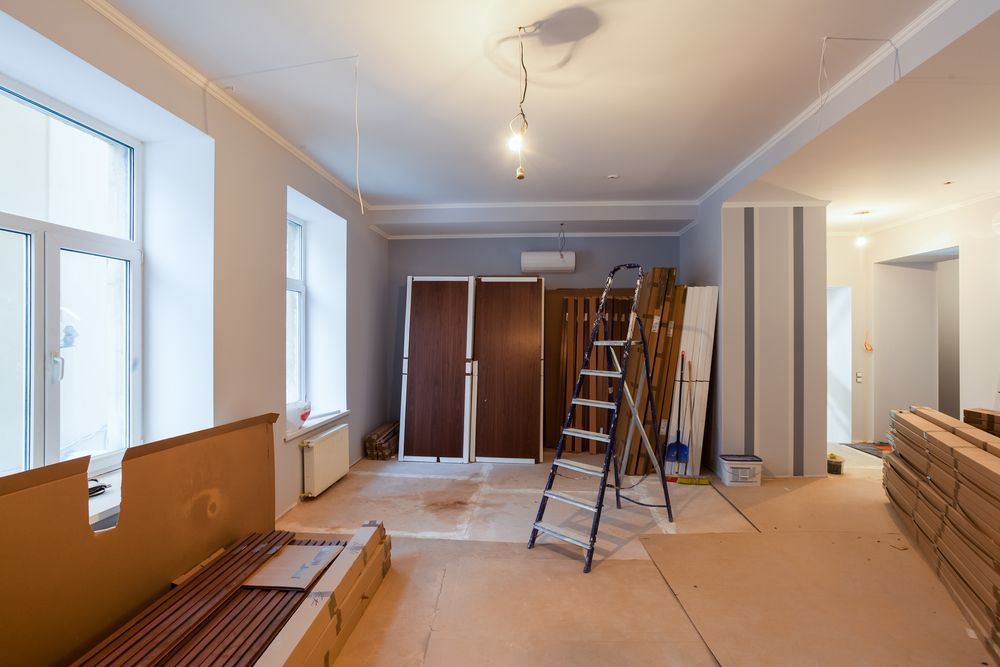 Room under renovation, showing windows, doors, ladder, and construction materials.
