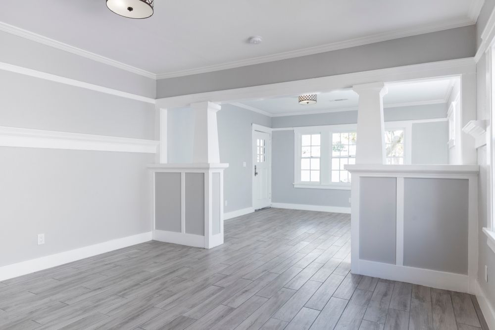 Empty, newly renovated room with gray wood-look floors, white trim, and pale gray walls.