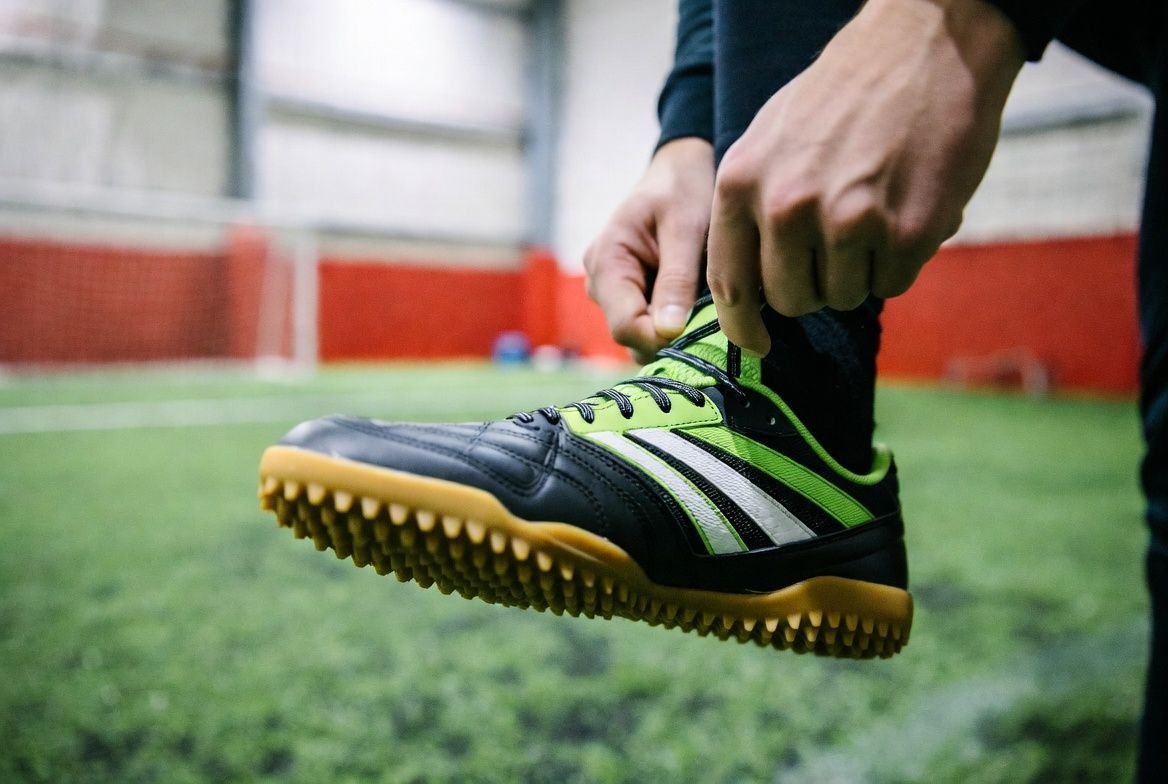Indoor soccer field with green turf, white lines, goals, and red wall accents.