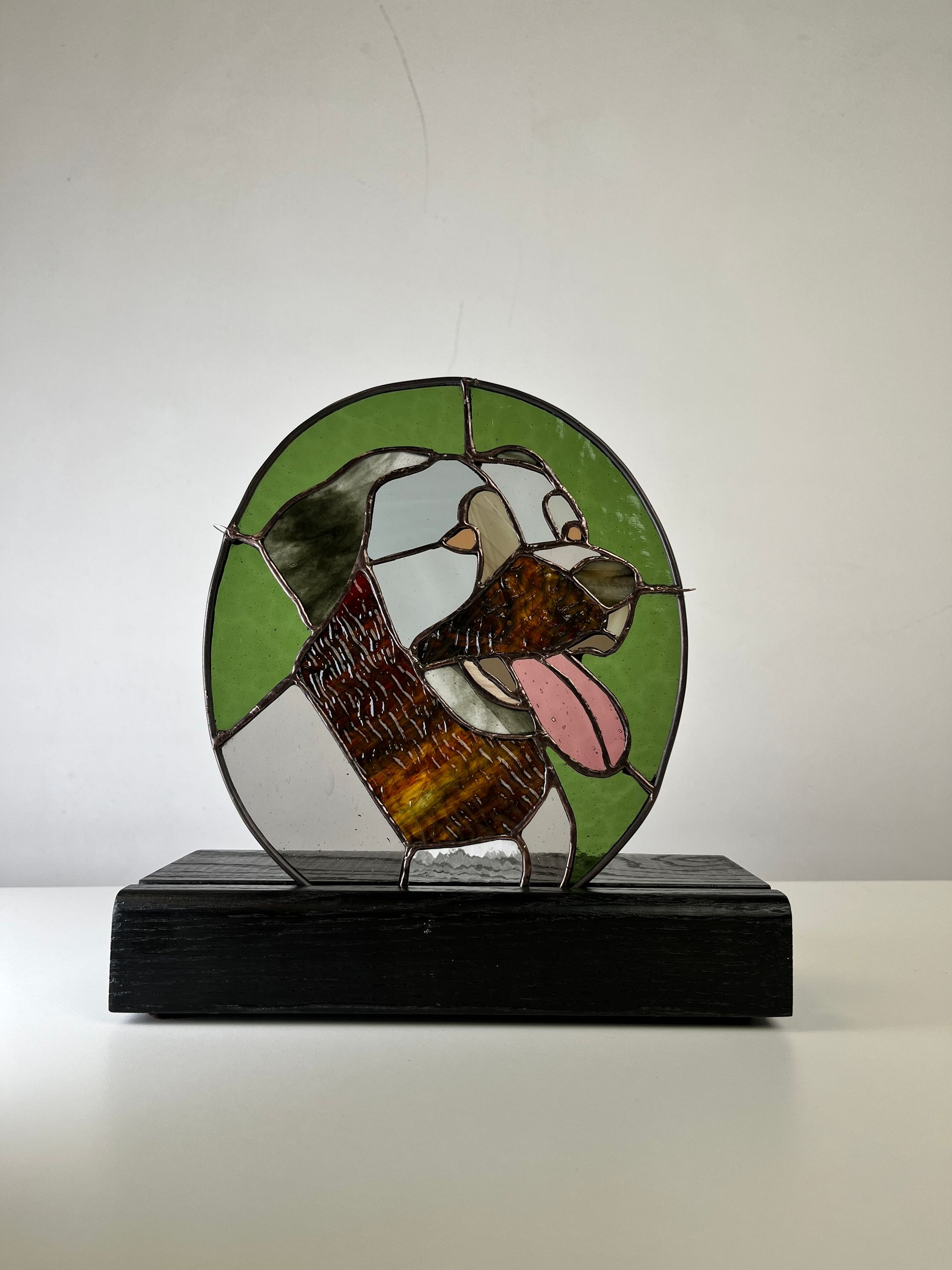 Tiffany-glasportret van een hond met uitgestoken tong, op een zwarte voet