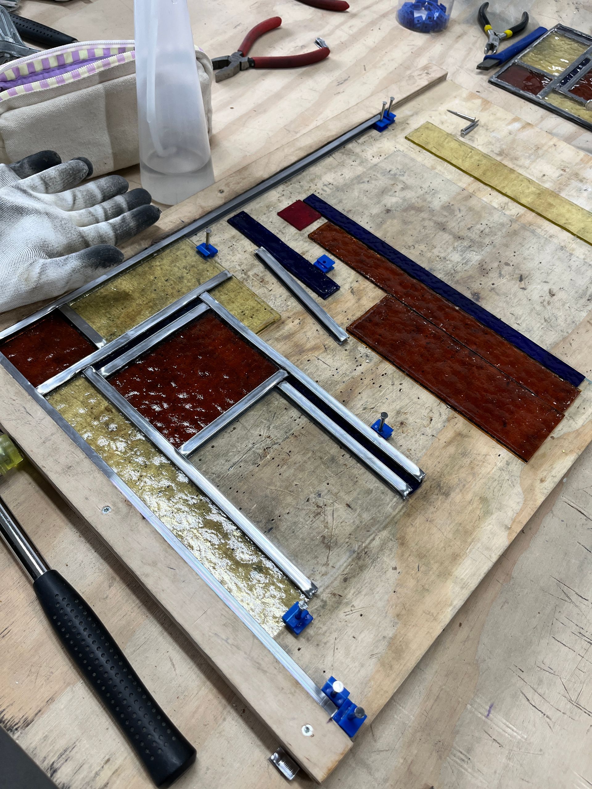 Glas-in-loodpaneel in de maak op de werkbank, met gereedschap ernaast
