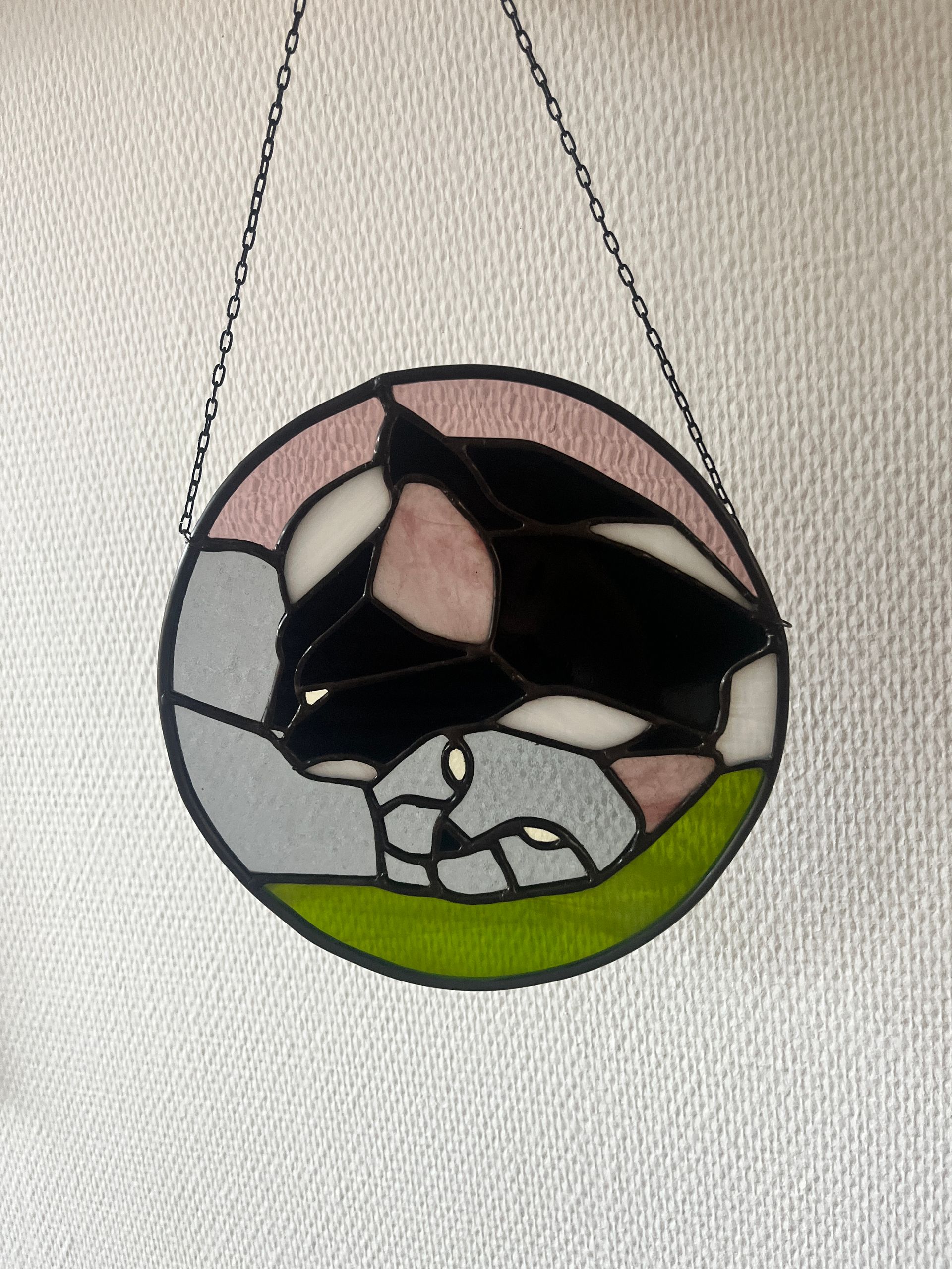 Rond Tiffany-glaspaneel van een slapende zwart-witte kat, aan een kettinkje