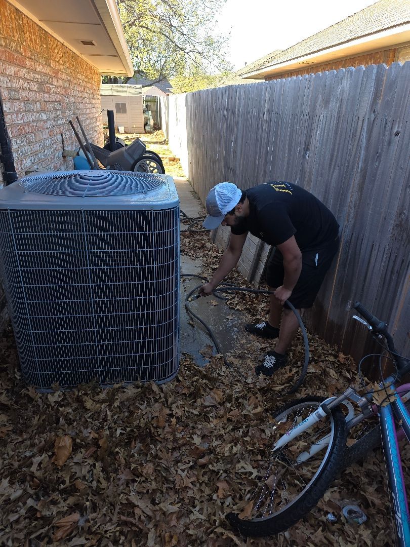 Technician working on HVAC unit beside a house in a narrow, leaf-covered alley