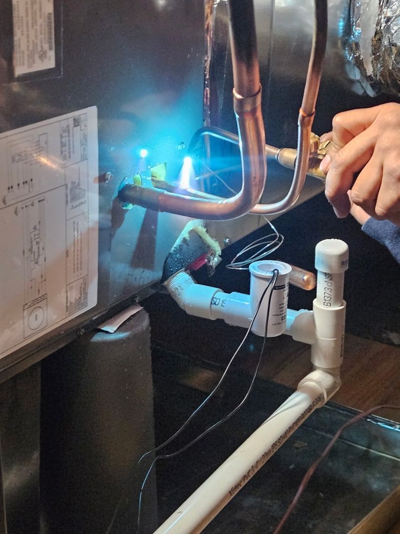Technician adjusting copper pipes in a dim boiler room, with blue inspection light shining on the equipment