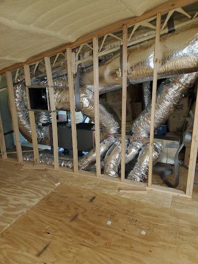 HVAC ductwork installation in a framed wall cavity, with exposed plywood flooring and spray foam insulation.