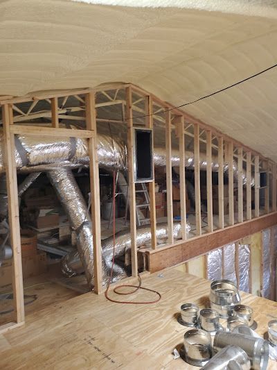 Attic interior with exposed ductwork, wooden framing, plywood floor, and spray foam insulation.