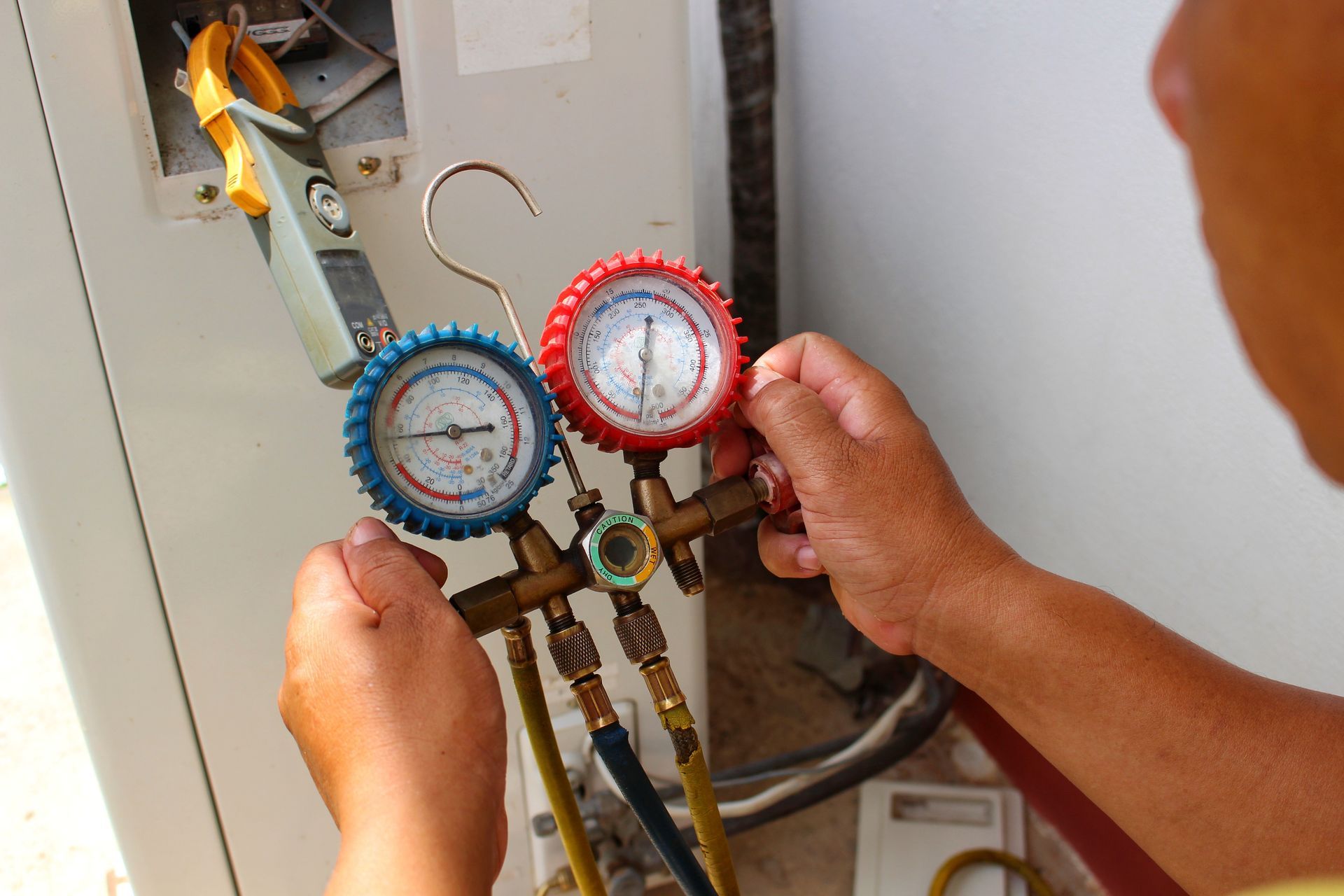 A technician uses a manifold gauge set and a clamp meter to service the outdoor unit of an air conditioner.