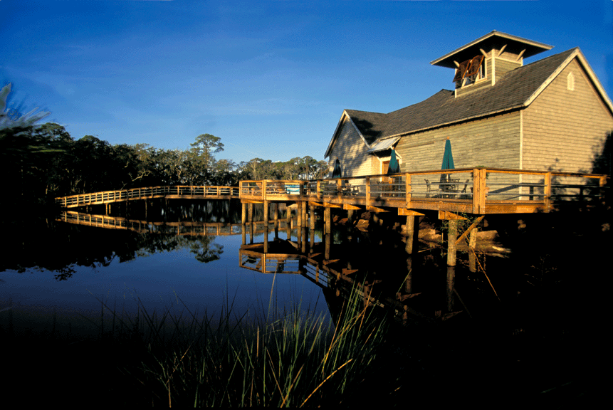 Swimming pool flanked by trees and small stone buildings under a wooden pergola.