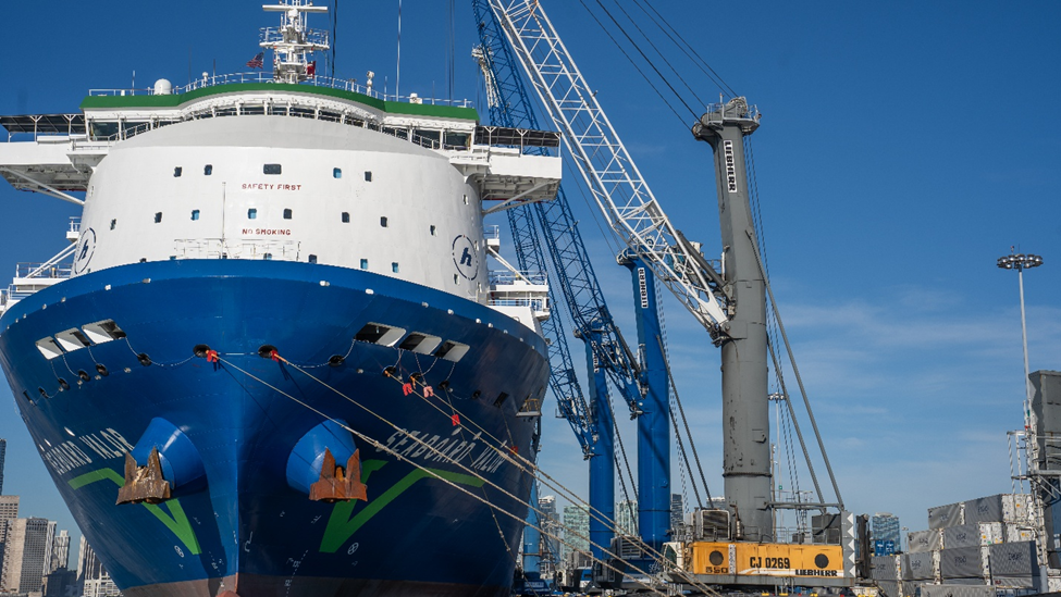 Gran barco azul y blanco atracado en un puerto, con grúas y maquinaria portuaria cerca