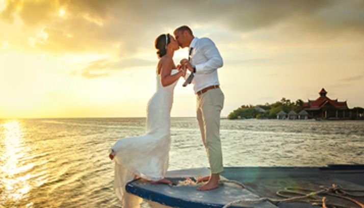Bride and groom kissing at sunset on a pier over water.