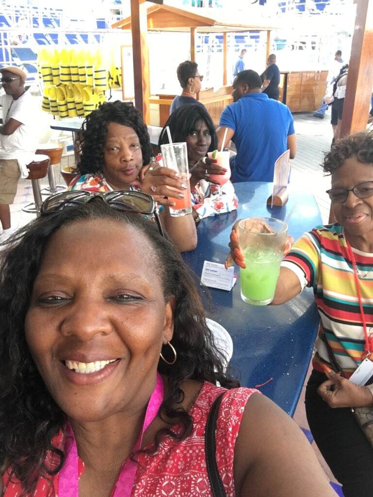 Four women on a boat deck, toasting drinks. One woman smiles at the camera.