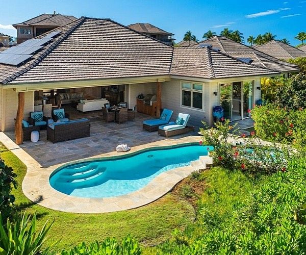 House with pool, patio, lounge chairs, and lush green landscaping on a sunny day.
