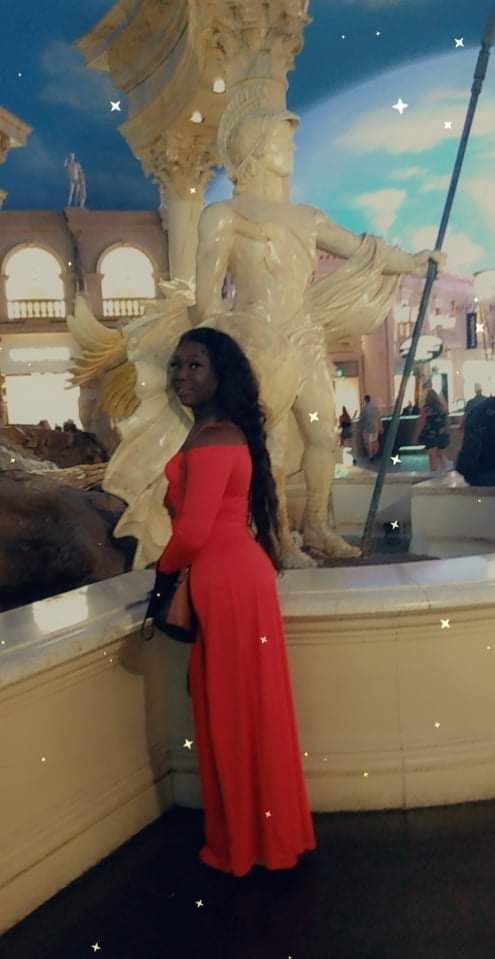 Woman in red dress poses by a statue in an ornate building.