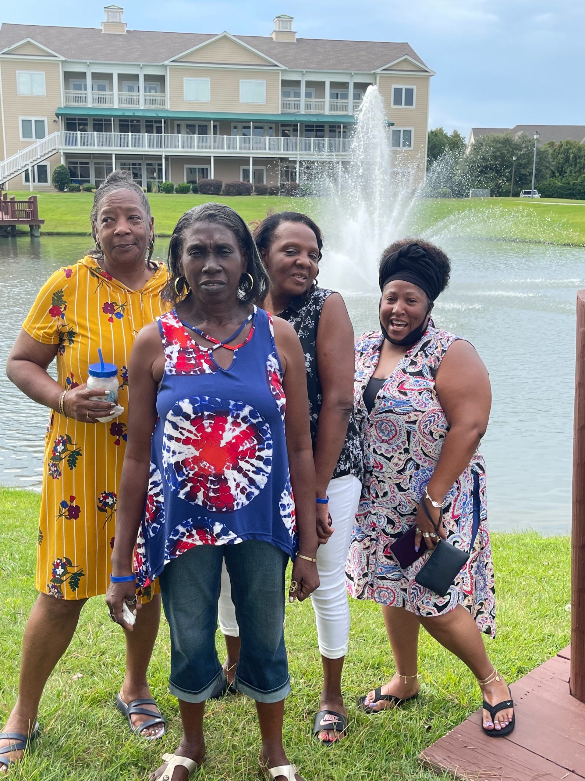 Four Black women pose near a fountain and pond in front of a building.