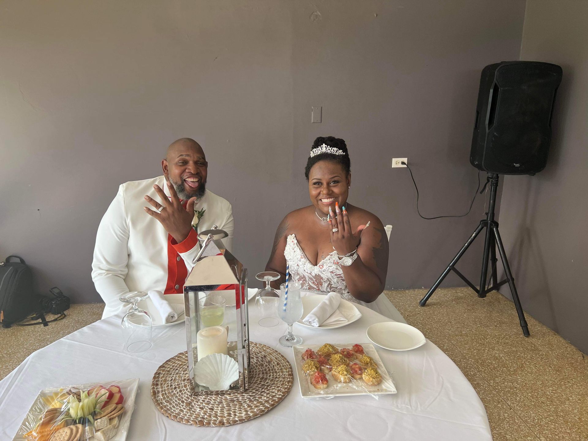 Newlyweds at a wedding reception, showing off their rings at a table.