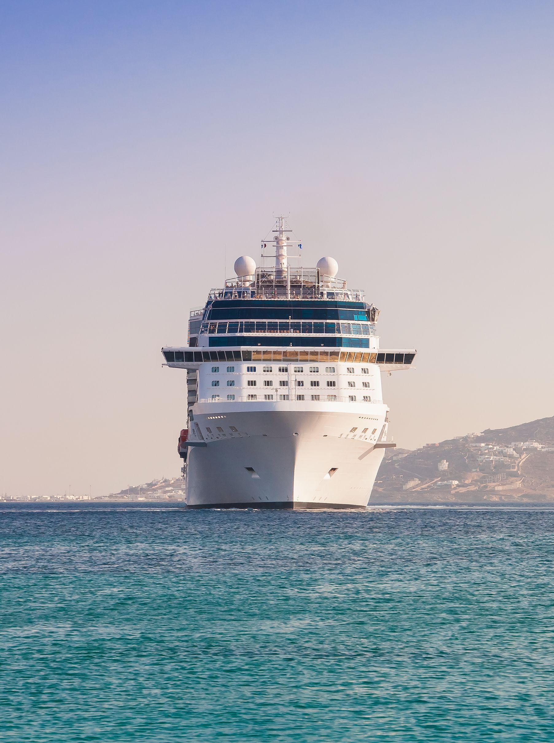Cruise ship sailing on a blue sea, passing a distant coastline on a clear day.