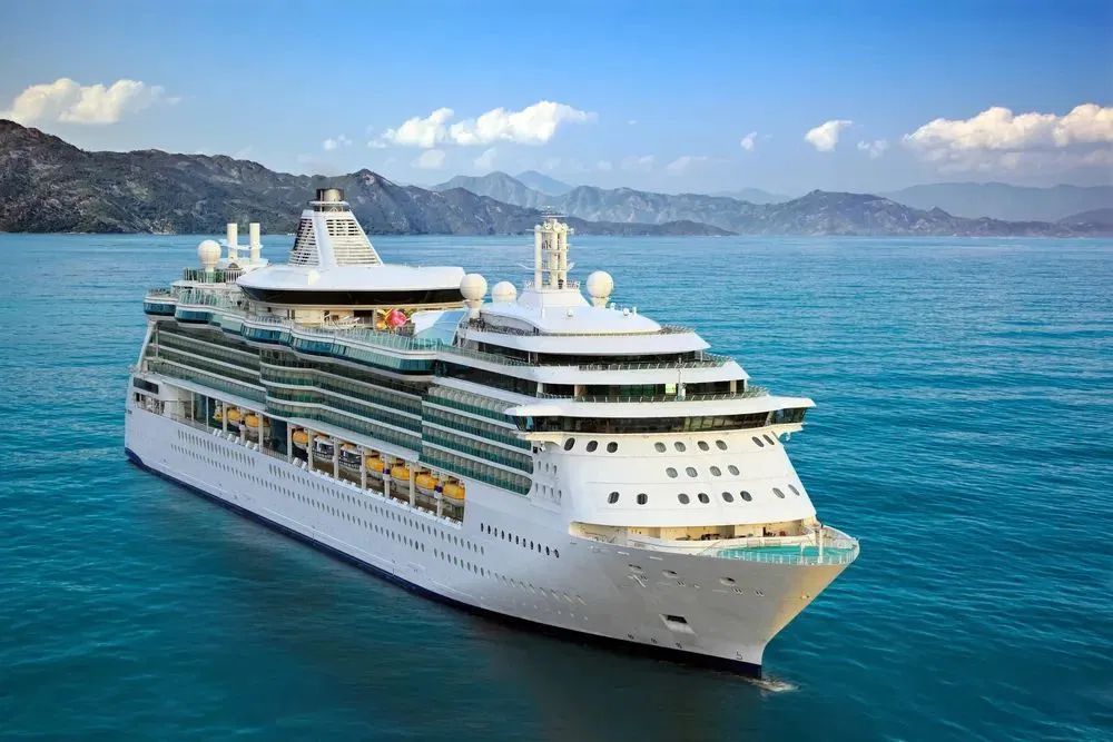White cruise ship sailing on blue water near rocky mountains under a clear sky