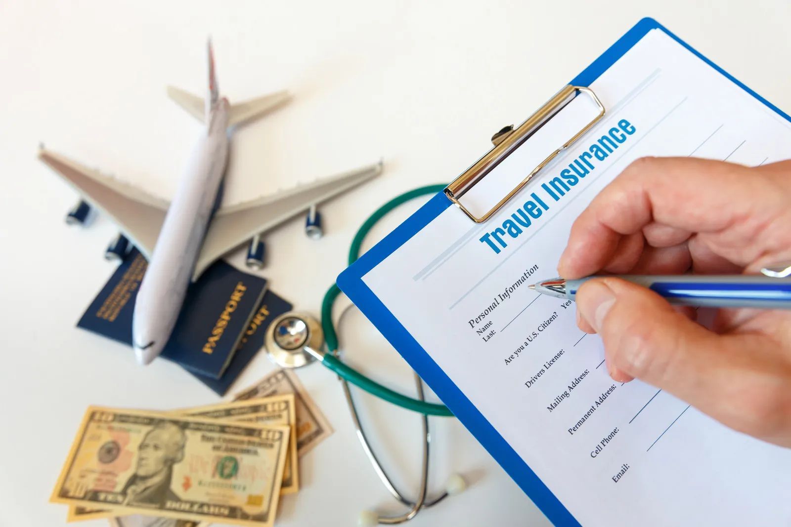 Travel insurance form with airplane, passport, stethoscope, cash, and a hand writing on a clipboard