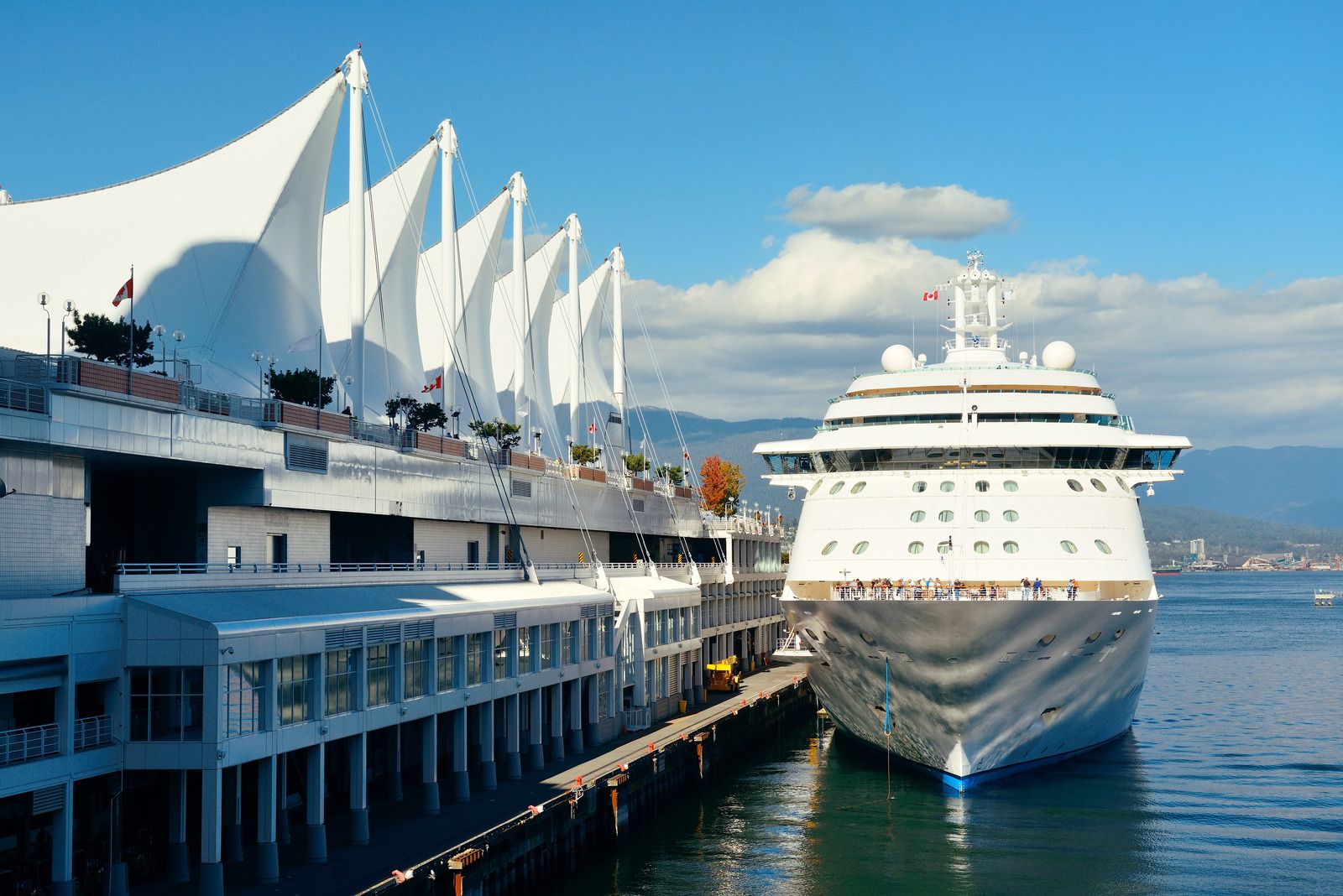Cruise ship docked at the Vancouver terminal with white sails and blue sky.