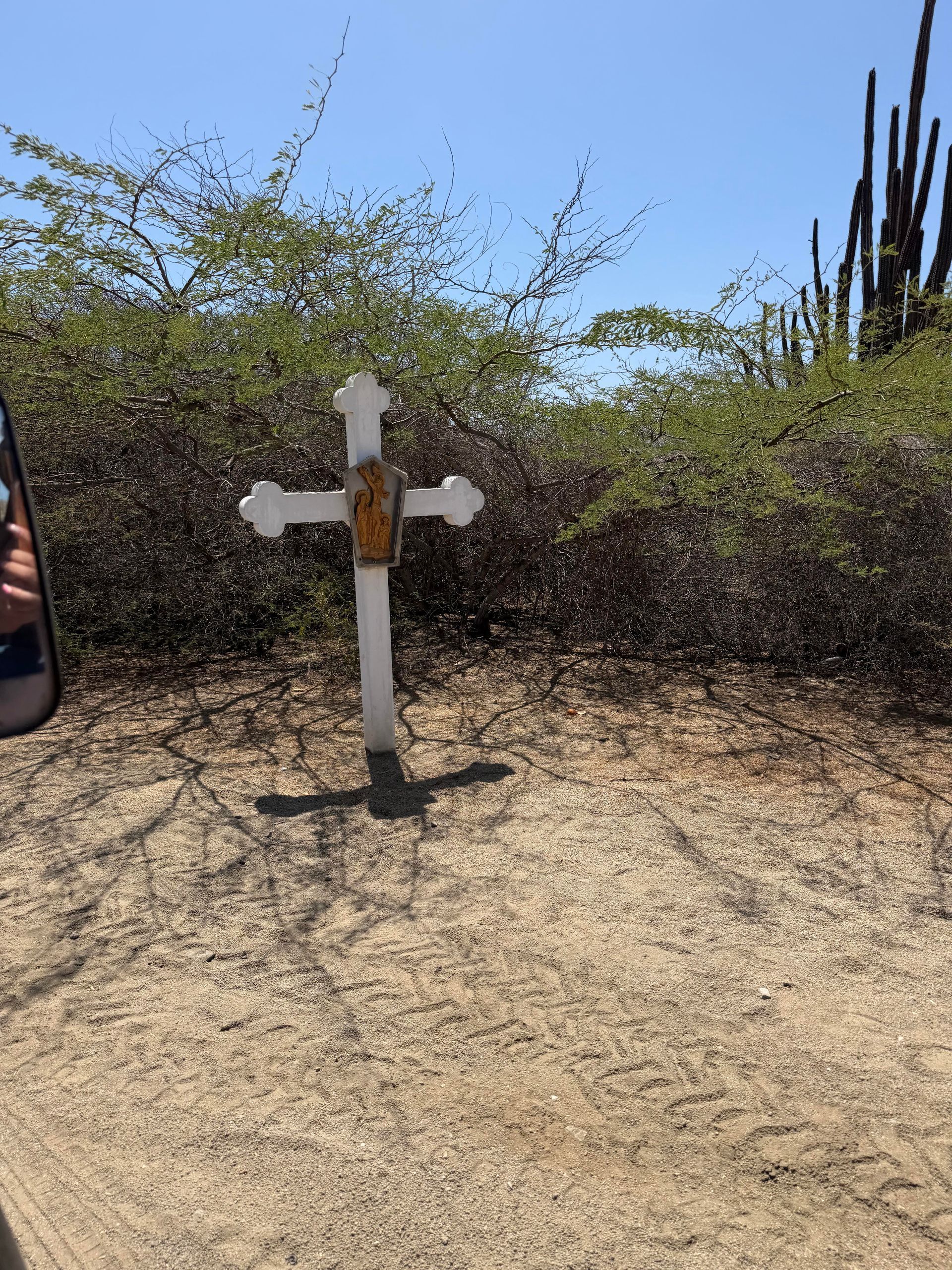 White cross memorial on a dry dirt path with shrubs and a blue sky background