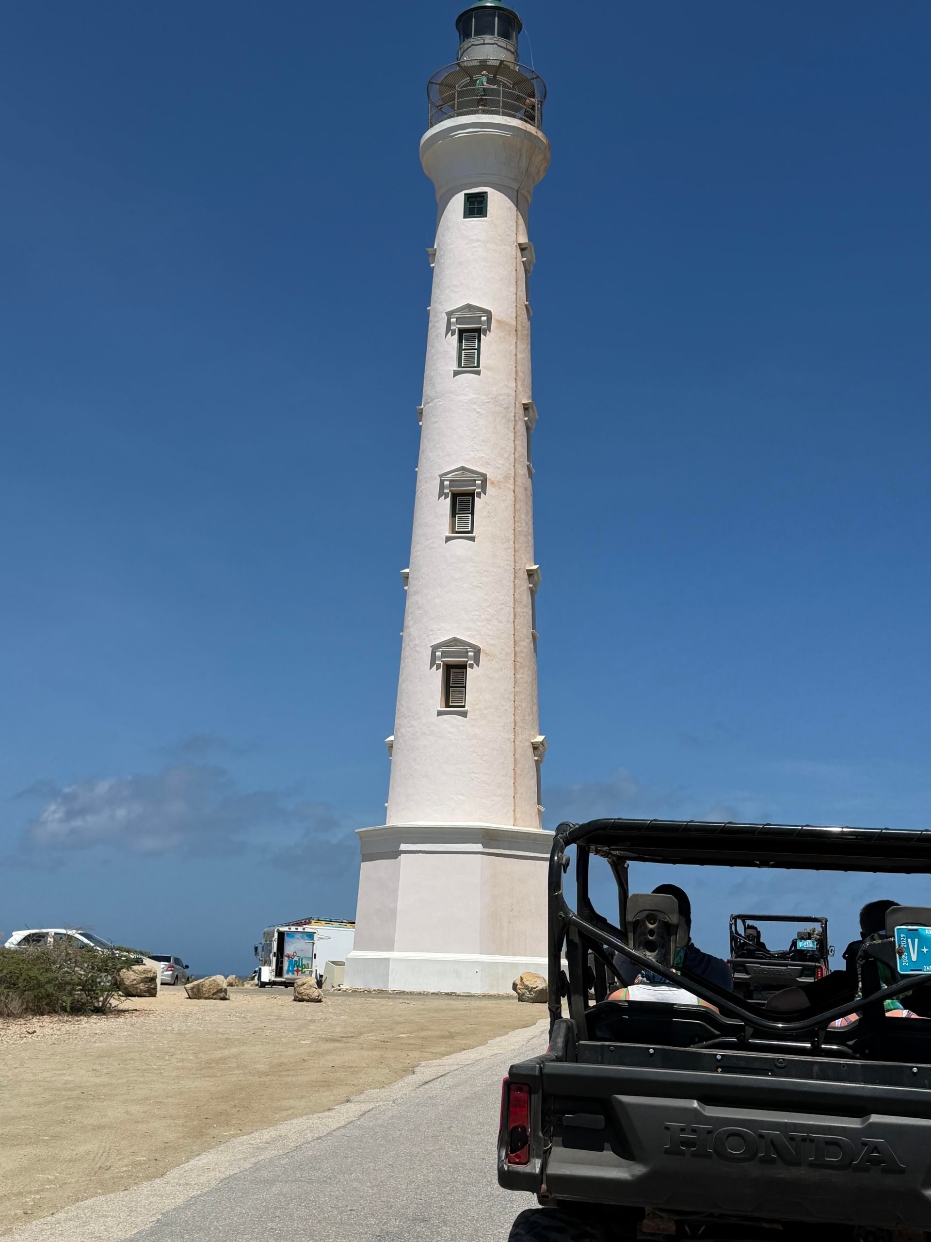 White lighthouse on a sandy coast with a blue sky and an open vehicle in the foreground