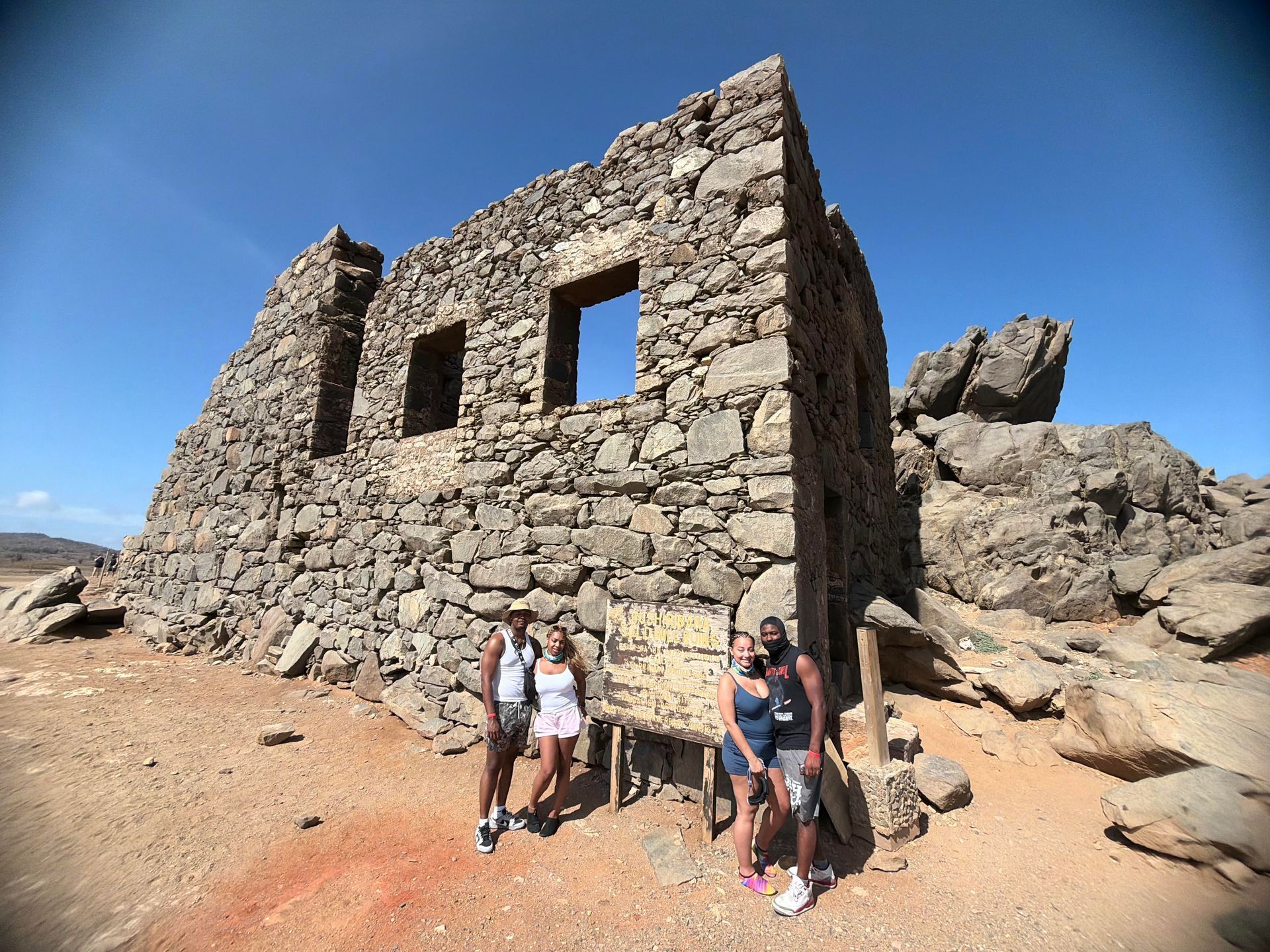 People standing beside a stone ruin in a rocky desert under a blue sky