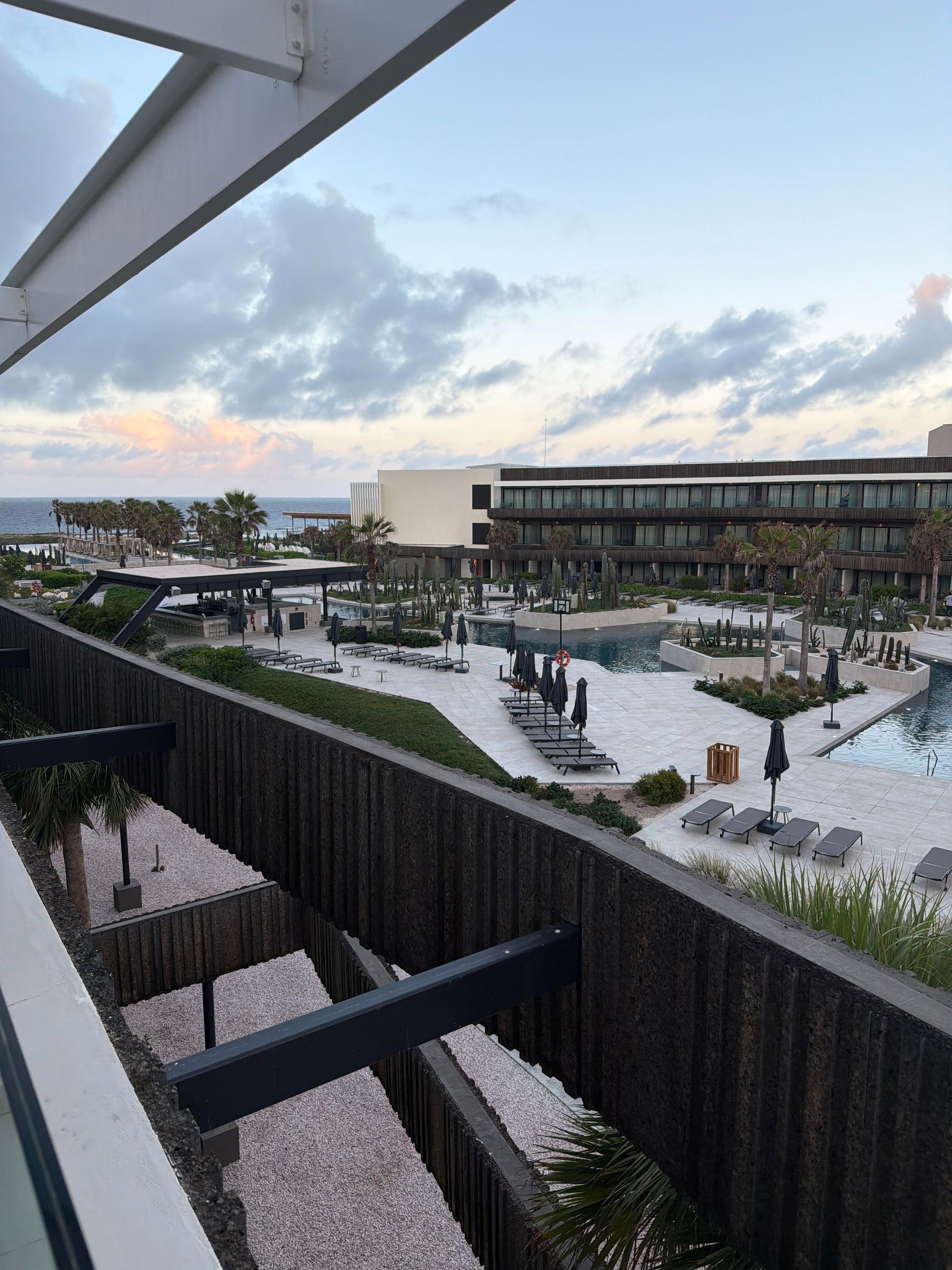 Modern resort courtyard with pools, palm trees, and lounge chairs at dusk