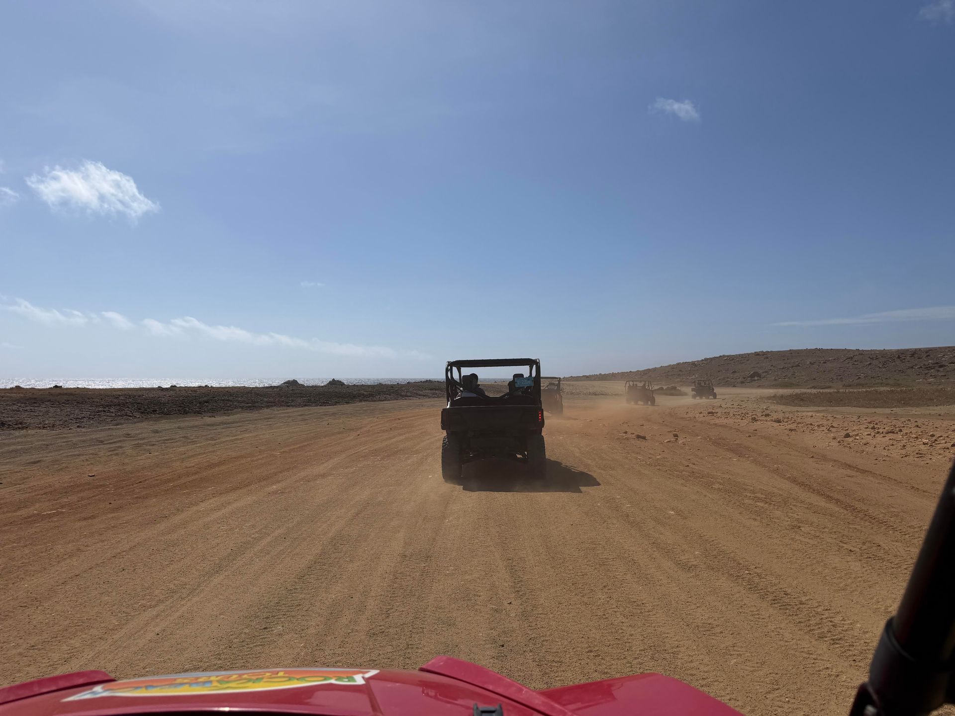 Off-road vehicle driving on a dusty desert road under a clear blue sky