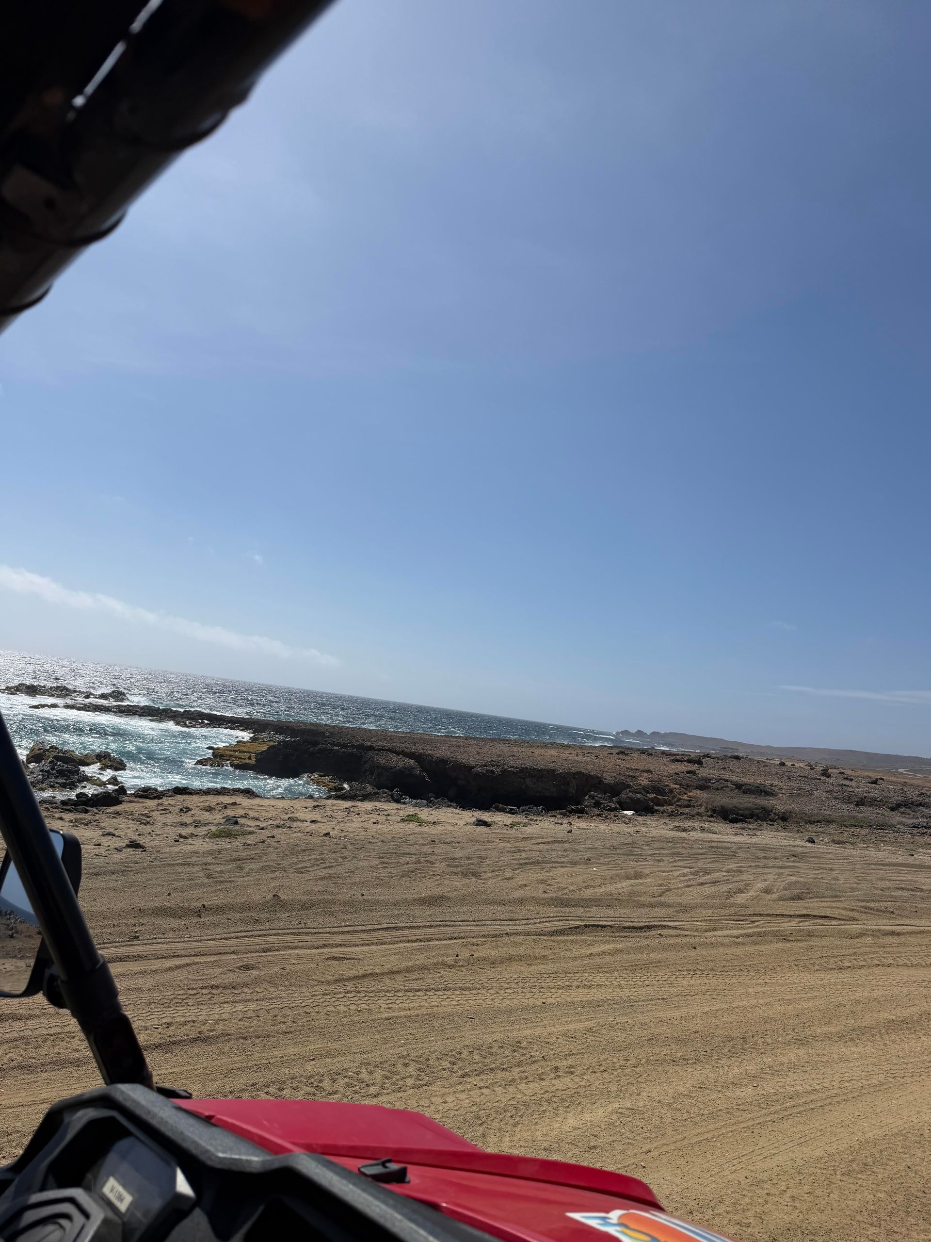 Beach view from a vehicle, with blue sky, rocky shore, and sparkling ocean ahead