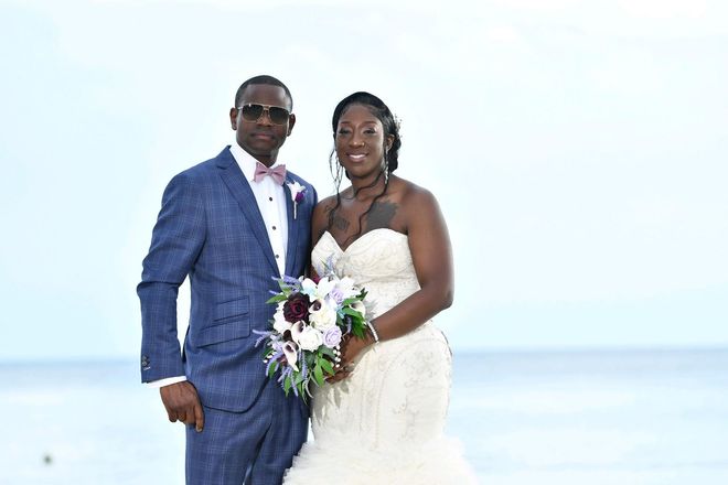 Groom in blue suit and bride in white gown pose at the beach, holding a bouquet.