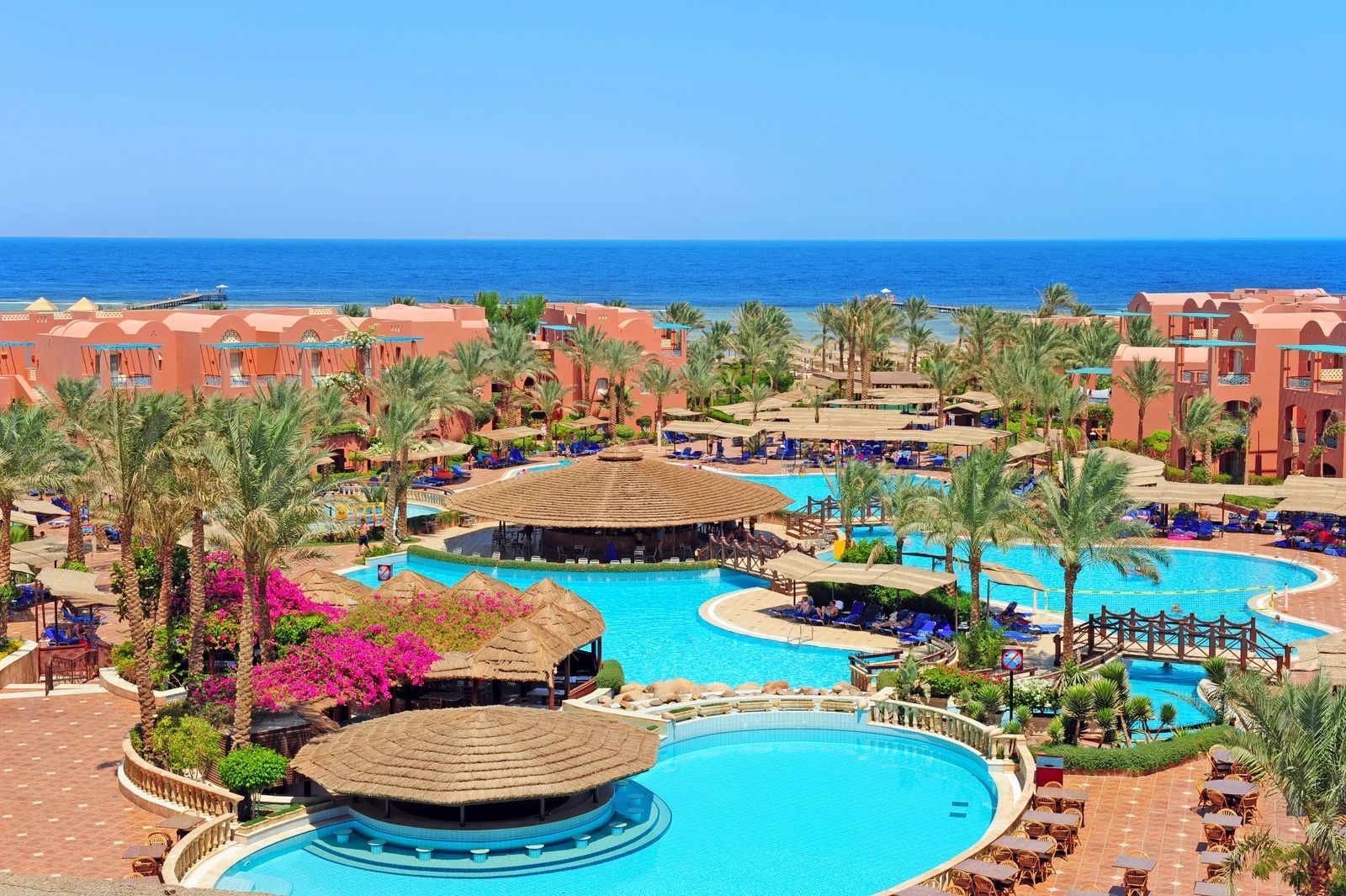 Resort pool complex with blue pools, palm trees, and ocean view under a clear sky
