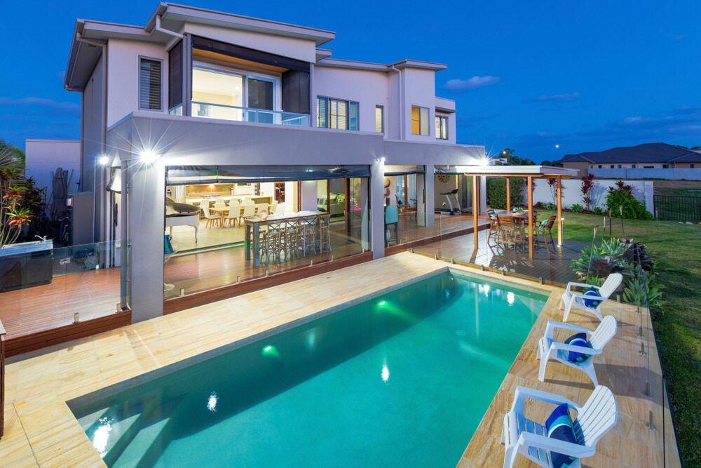 Two-story House With a Pool, Outdoor Kitchen, and Lounge Chairs at Dusk — Dean Thomas Pools in Palm Cove, QLD