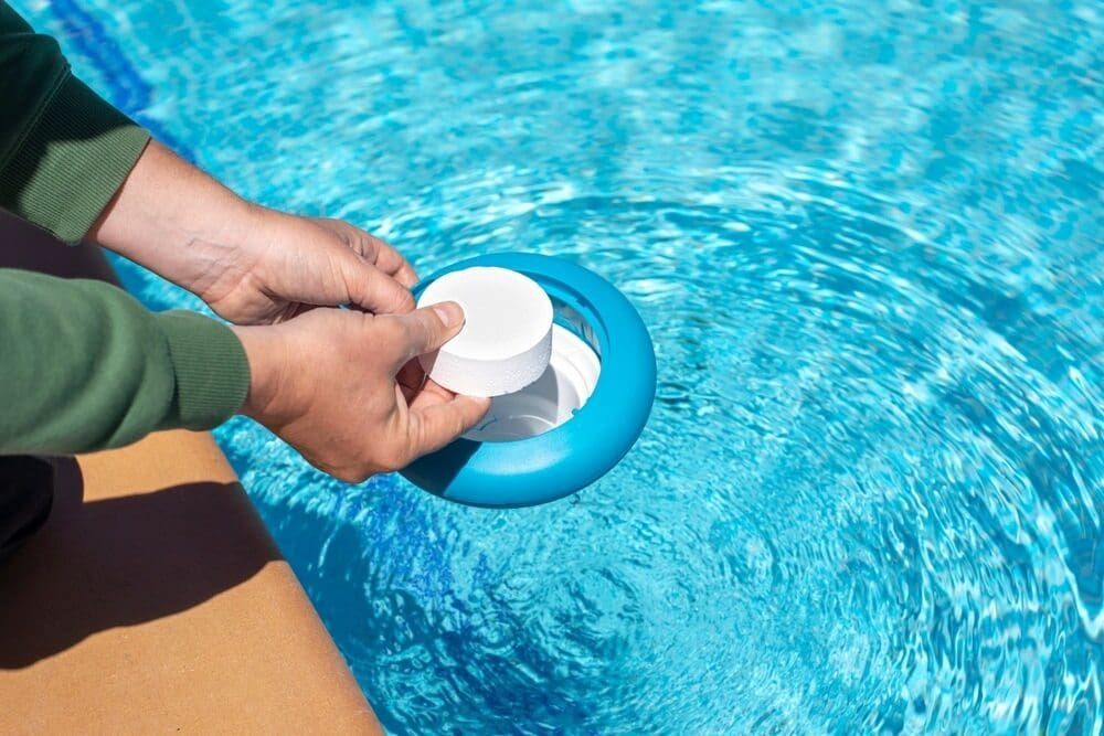 Hands Placing a White Chlorine Tablet Into a Blue Floating Pool Chemical Dispenser — Dean Thomas Pools in Manunda, QLD