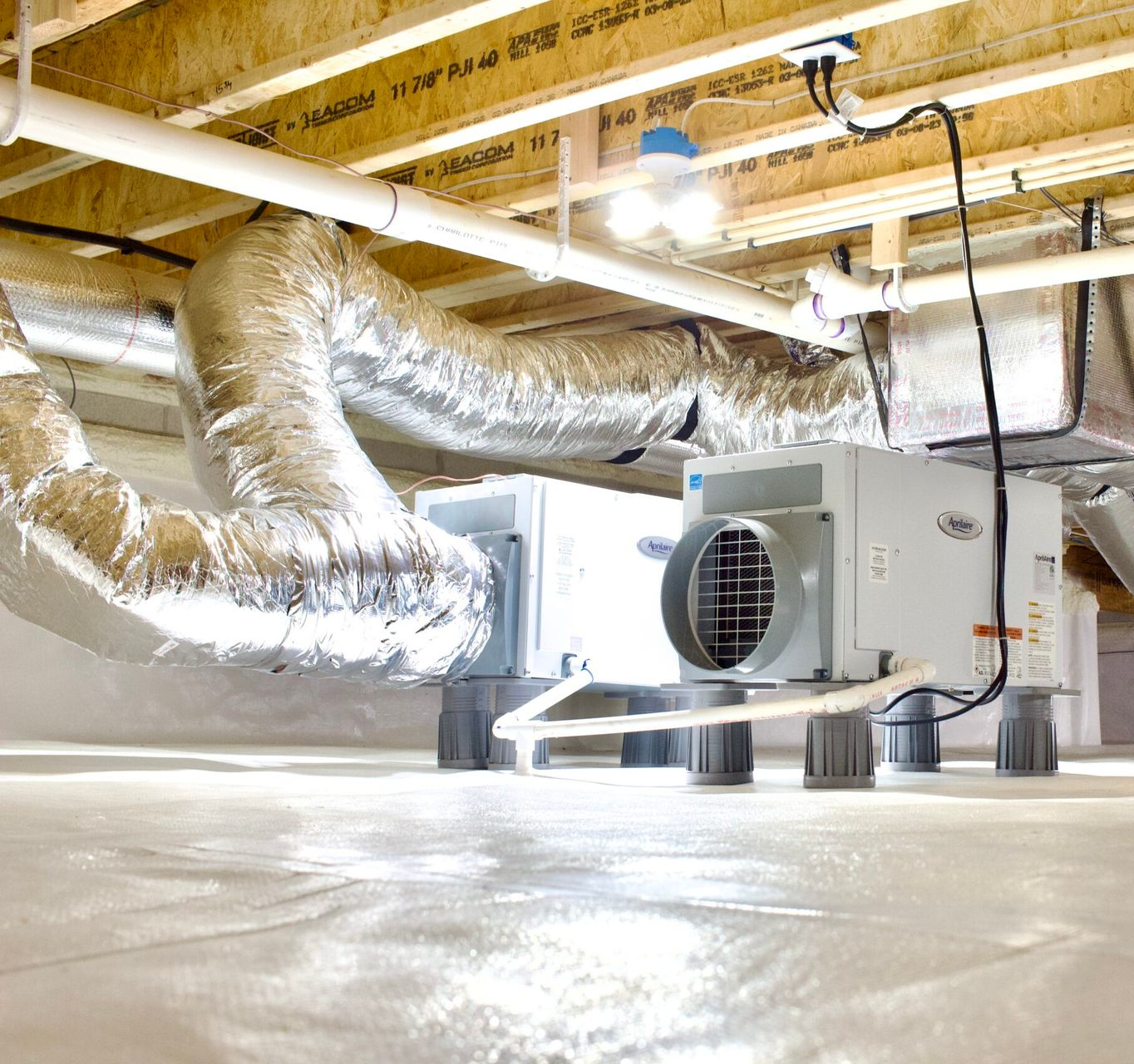 Dehumidifier in a crawl space with ductwork and insulation, on a white surface.