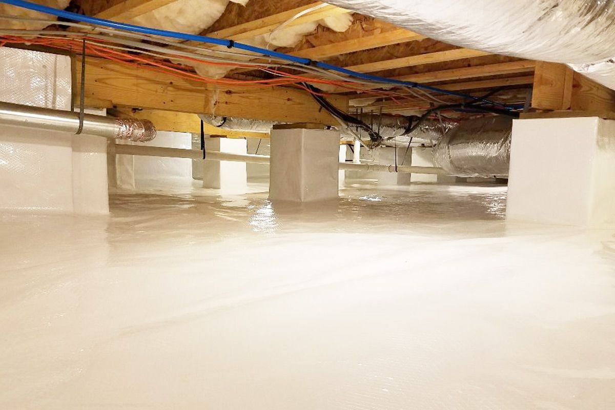 Crawlspace with white vapor barrier, supporting piers, ductwork, and wiring beneath a wooden floor.