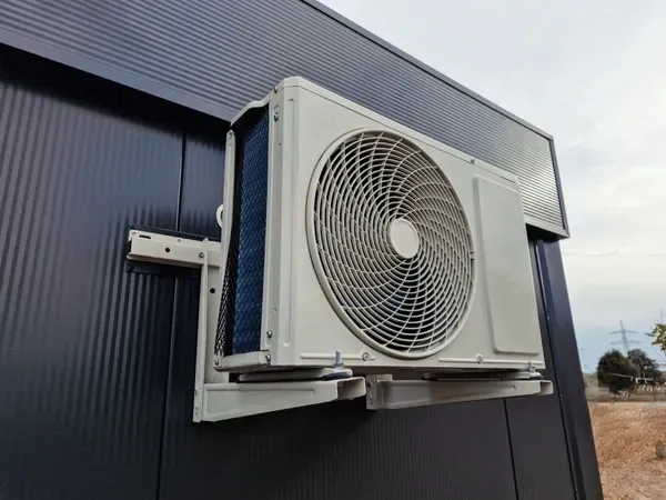 An air conditioning unit is mounted on the black exterior wall of a building.