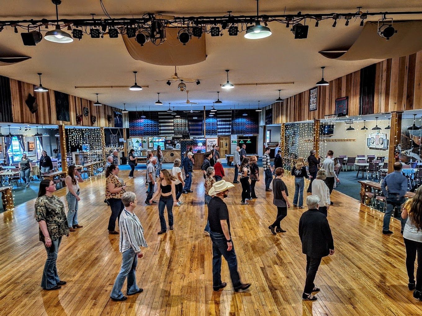 People dancing in a mirrored studio with wooden floors and overhead lights