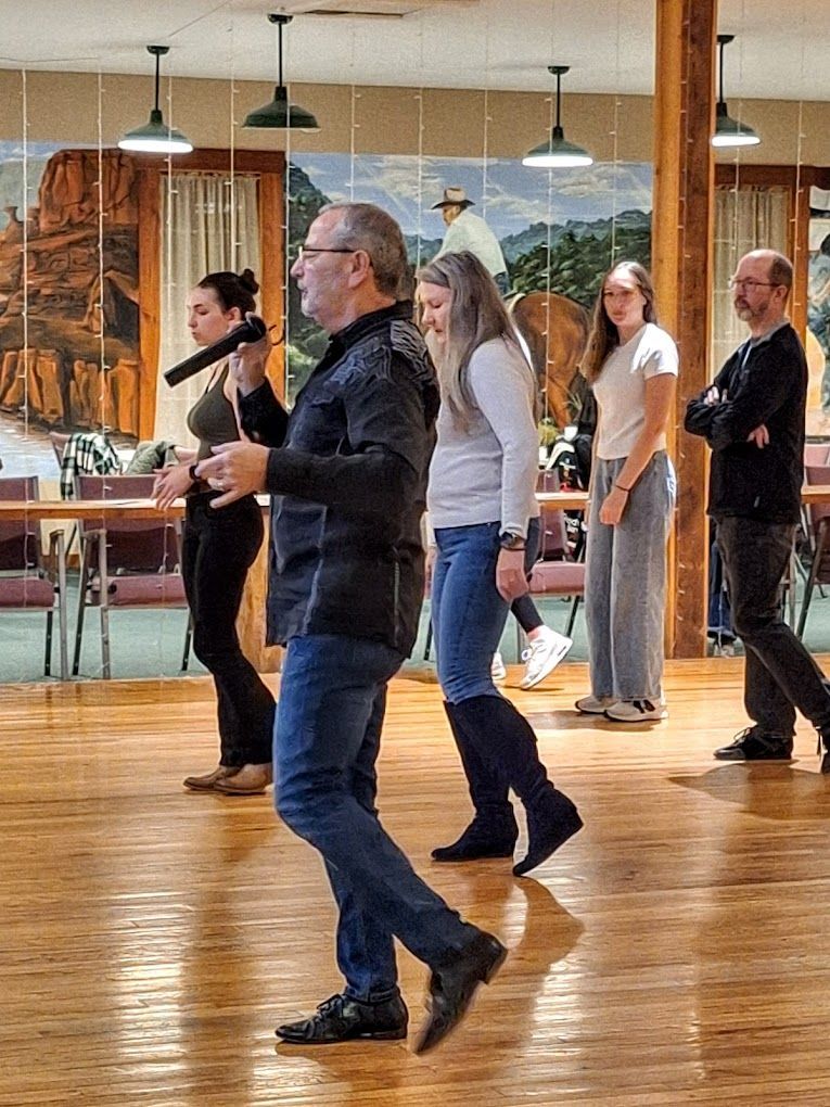 People dancing in a mirrored studio with wood floors and hanging lights