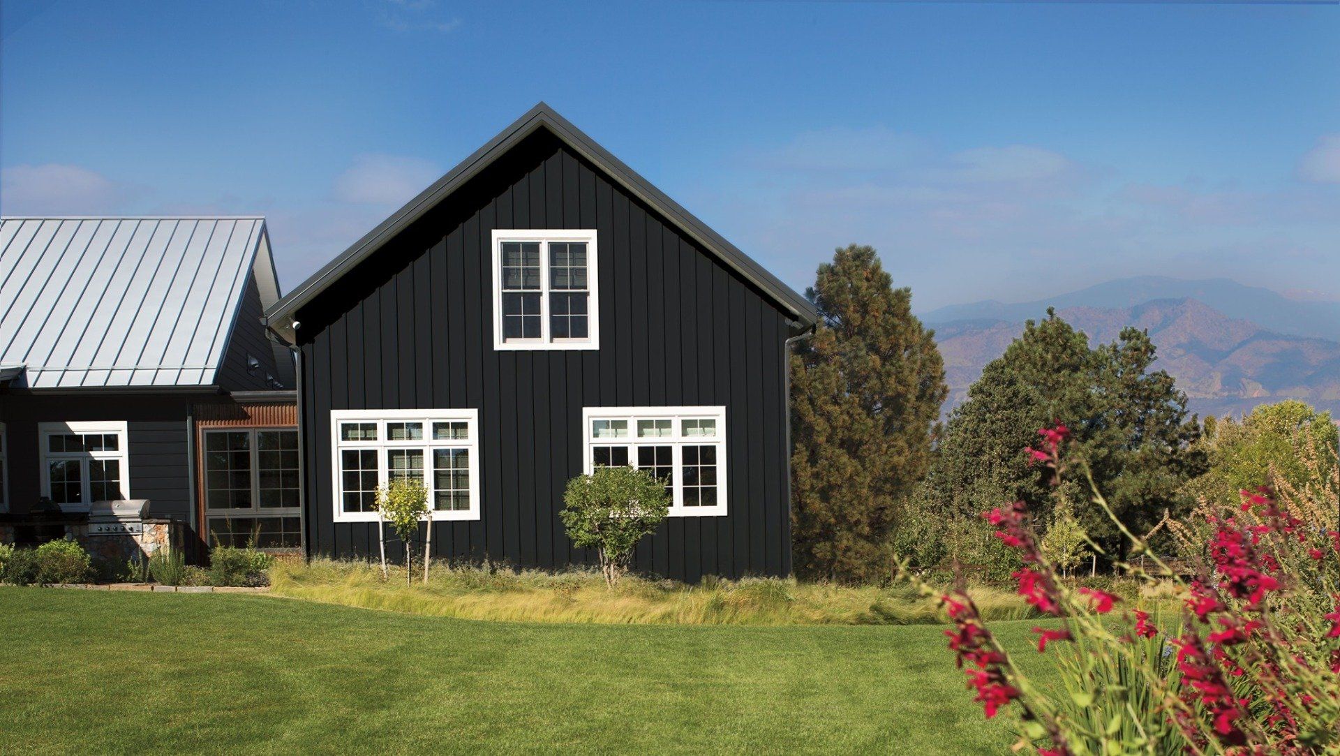 A black house with white windows is sitting on top of a lush green field.