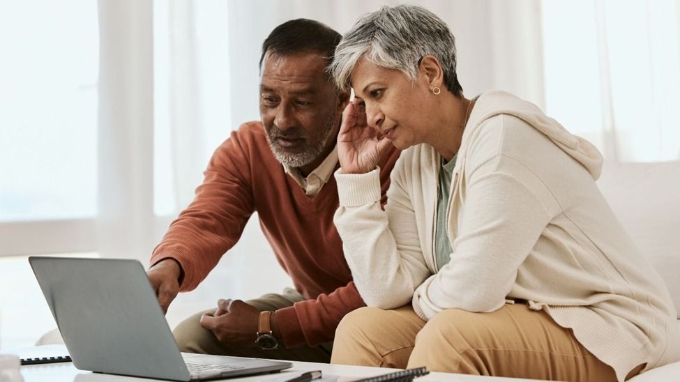 Two people leaning over a laptop on a couch, focused on the screen in a bright room.
