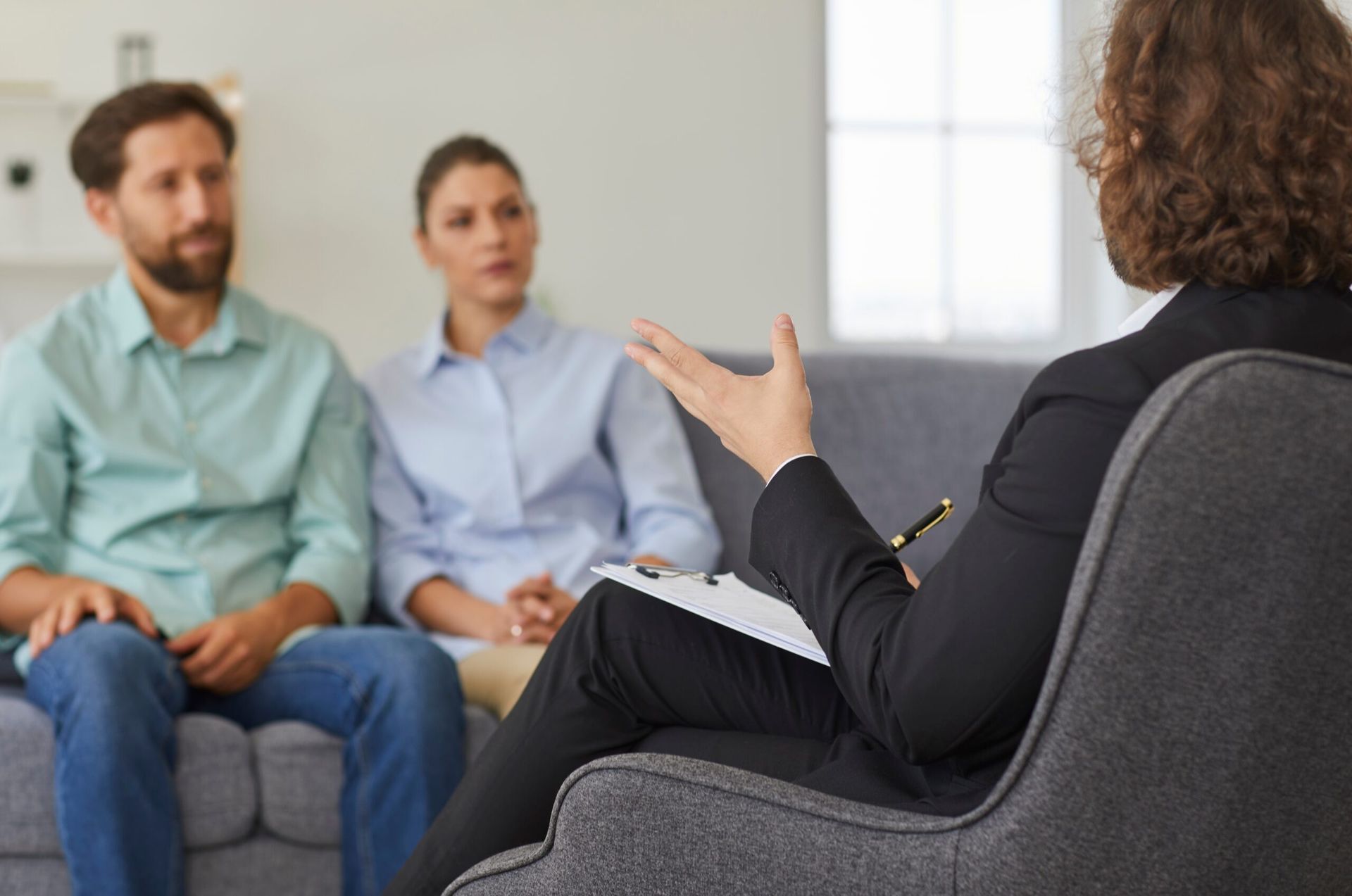 Counselor speaking to a seated couple during a therapy session in a bright office