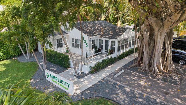 Corner house with white siding and green trim beside a large tree and sidewalk, viewed from above
