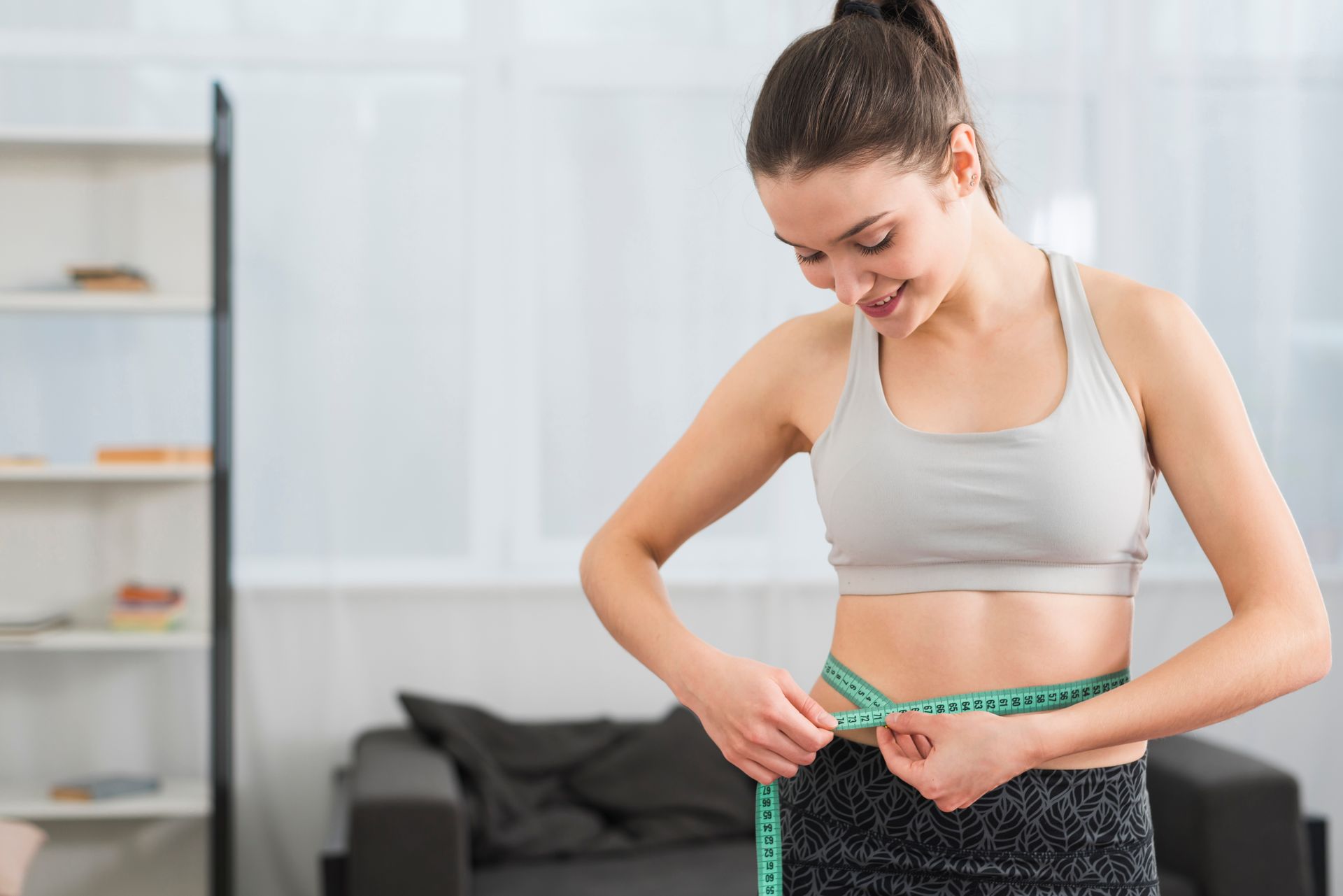 Woman measuring her waist with a tape measure in a bright living room
