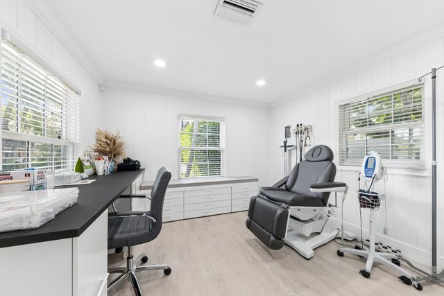 Bright medical exam room with exam chair, desk, stool, and equipment by windows