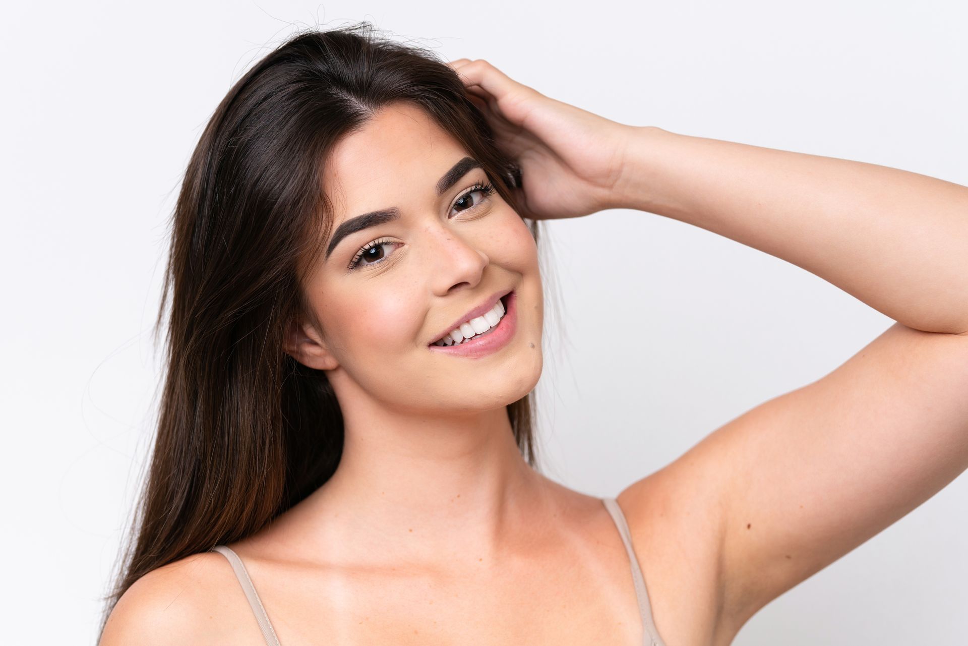 Smiling woman with dark hair posing against a light background, hand on her head