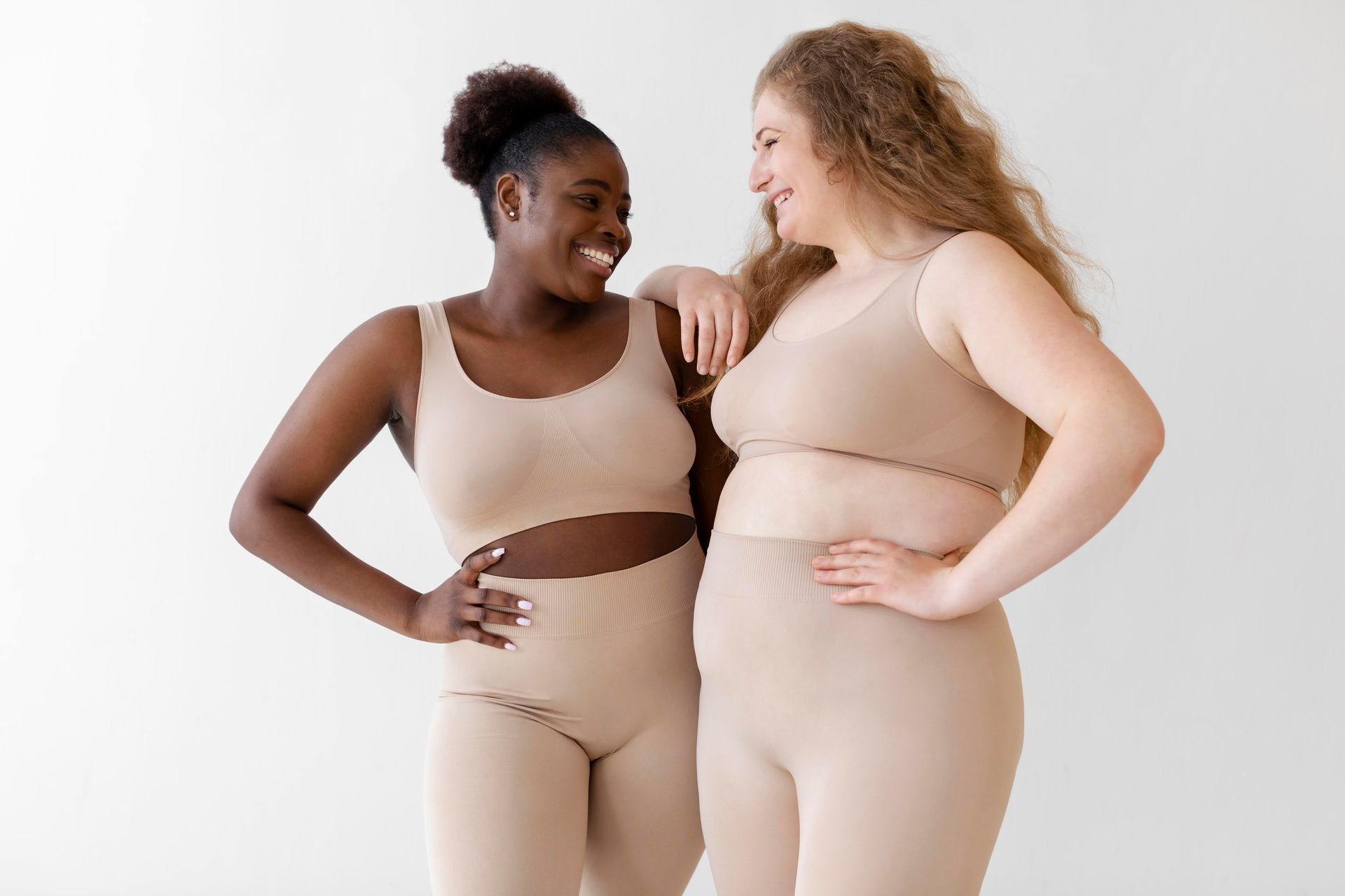 Two women in beige activewear smiling and posing against a white background