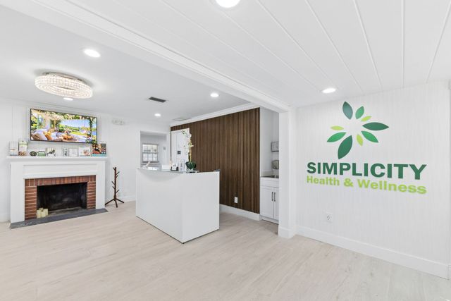 Bright clinic reception with fireplace, white desk, and Simplicity Health & Wellness logo on wall