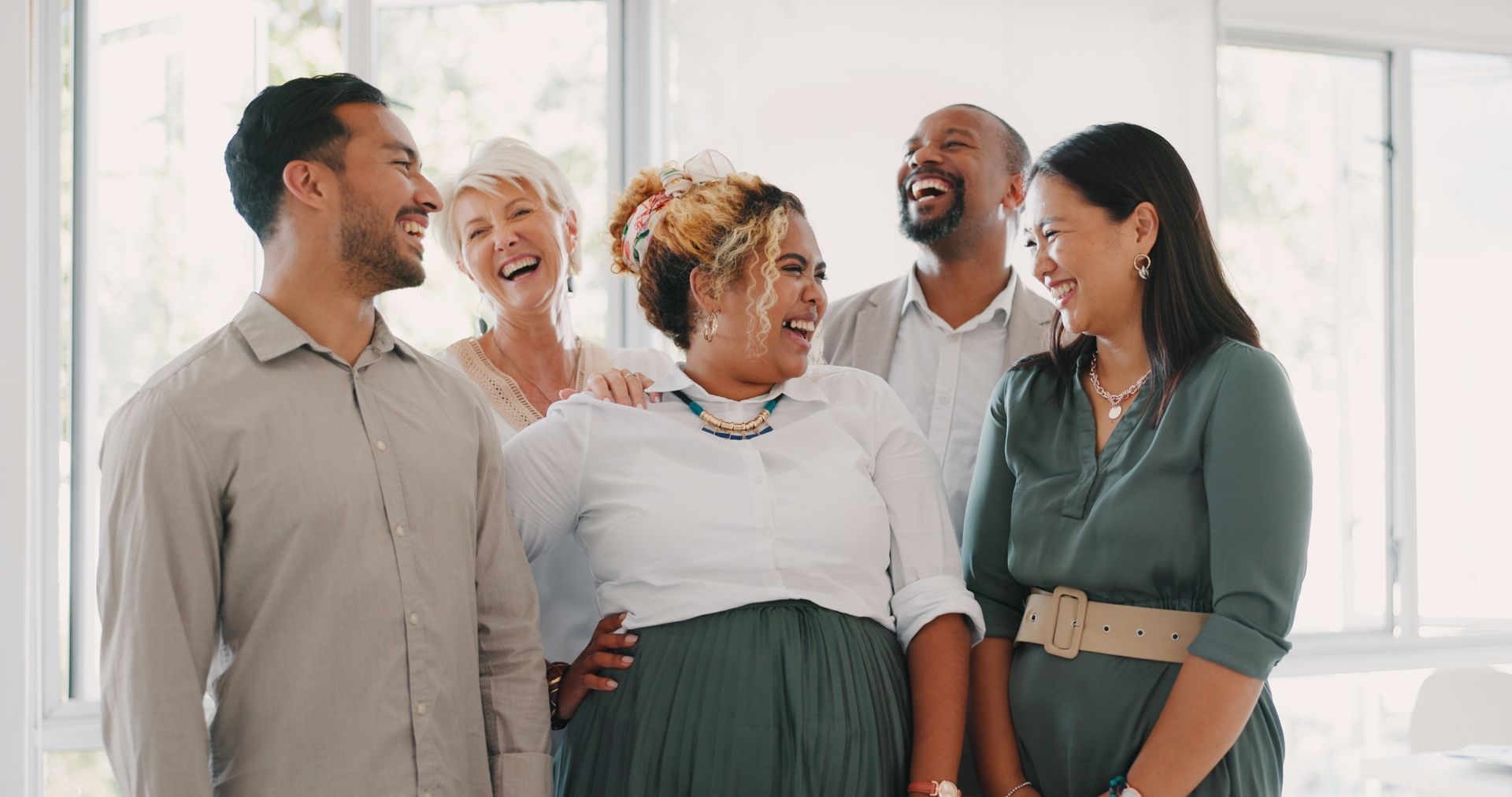 A group of five professionals in a bright office space laughing together during a collaborative meeting.