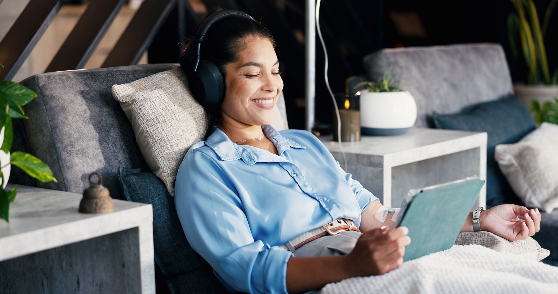 Woman relaxing on a couch with headphones, smiling while using a tablet in a cozy living room.